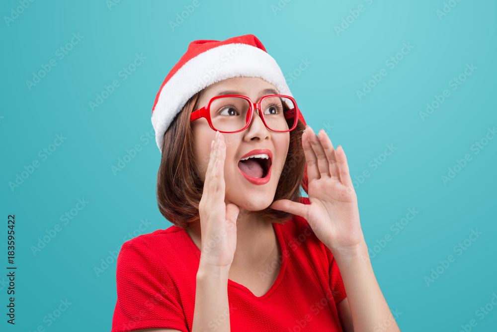 Smiling asian woman portrait with christmas santa hat shouting isolated on blue background.