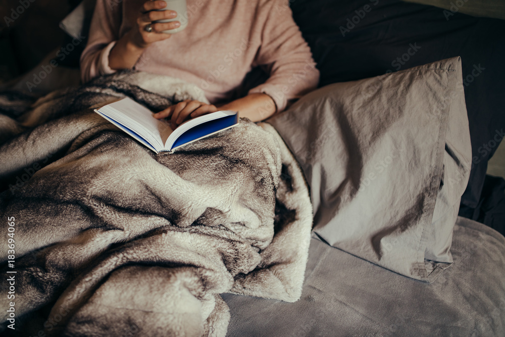 Woman on bed reading book and drinking coffee