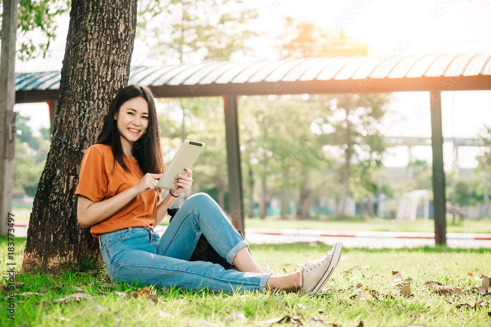 一个年轻或十几岁的亚洲女学生在大学里微笑着看书，看着平板电脑