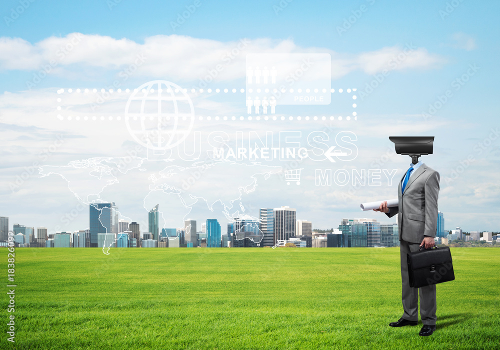 Camera headed man standing on green grass against modern cityscape