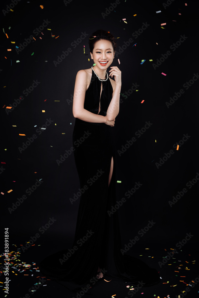 Asian woman with fashion makeup in luxury black dress while confetti falling on her.