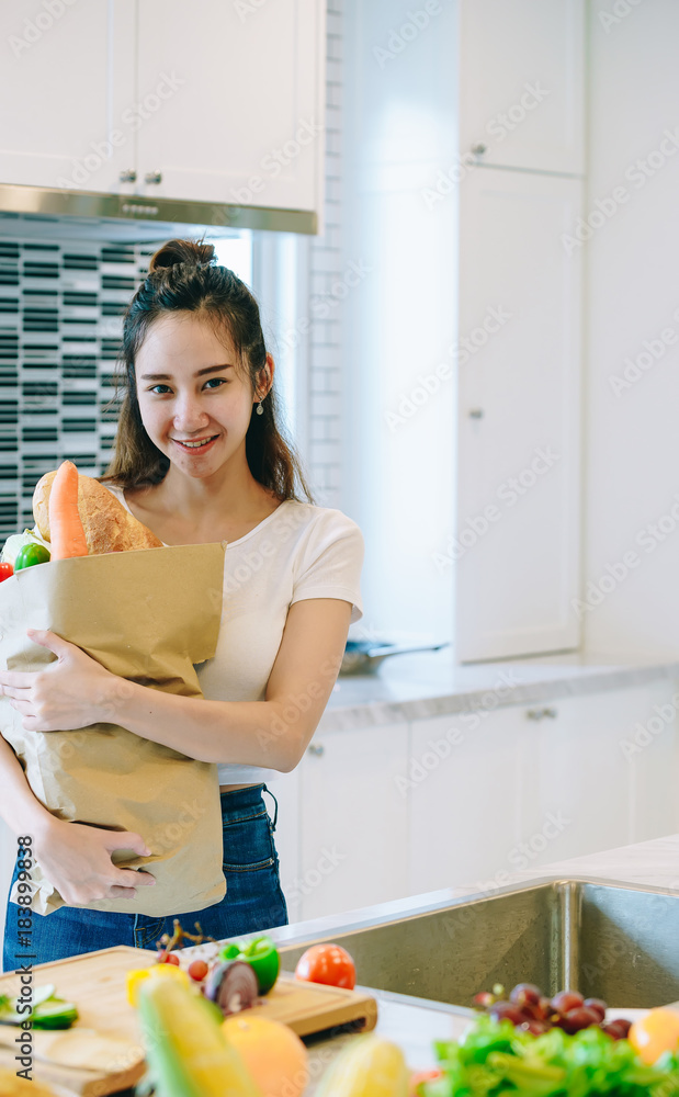 在她甜蜜的家里，一位亚洲妇女把水果装在纸袋里放在厨房里做晚饭。