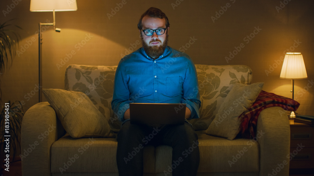 Portrait Shot of a Man Sitting on a Couch in His Living Room, Laptop on His Knees. Hes Working. Flo