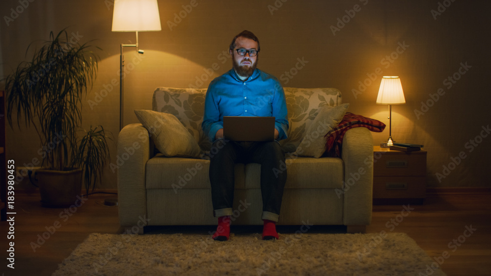 Portrait Shot of a Man Sitting on a Couch in His Living Room, Laptop on His Knees. Hes Working. Flo