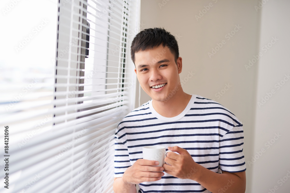 Portrait of a smiling man relaxing near window holding coffee cup