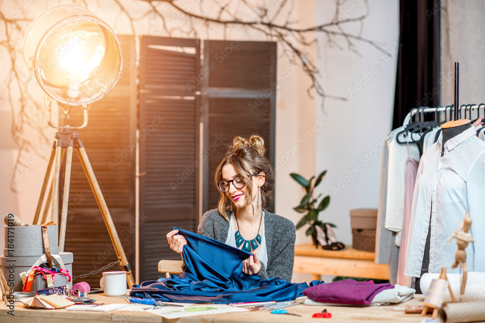 Young female fashion designer working with blue fabric sitting at the beautiful office with differen