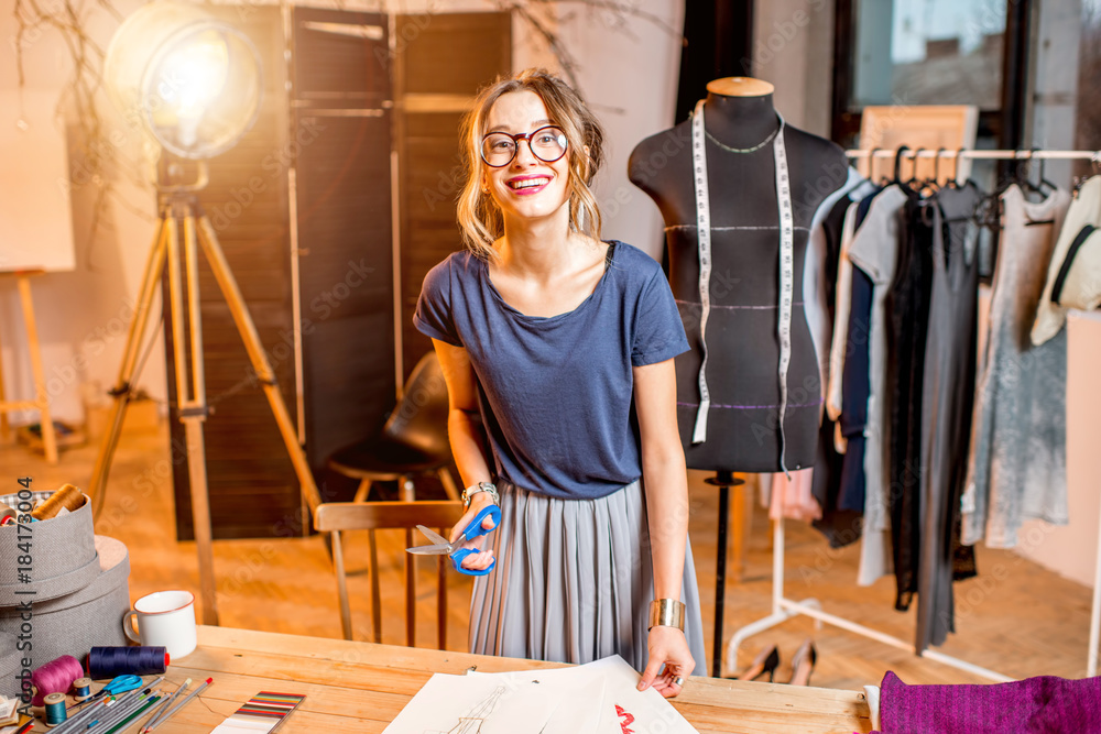 Young woman tailor working with scissors and drawings at the studio with different tailoring tools a