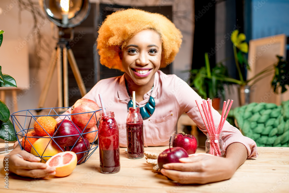 Portrait of a young african woman with fresh red fruits and smoothies sitting indoors at the cozy ho