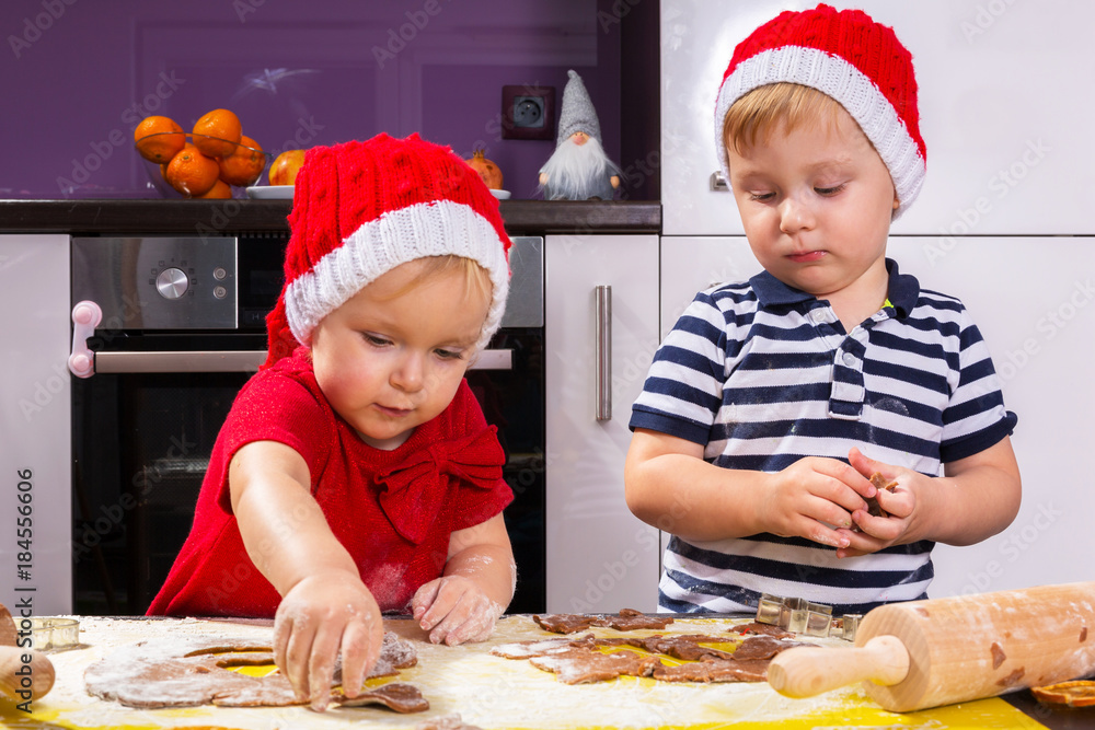 Cute little boy and girl twins preparing Christmas cookies in the kitchen