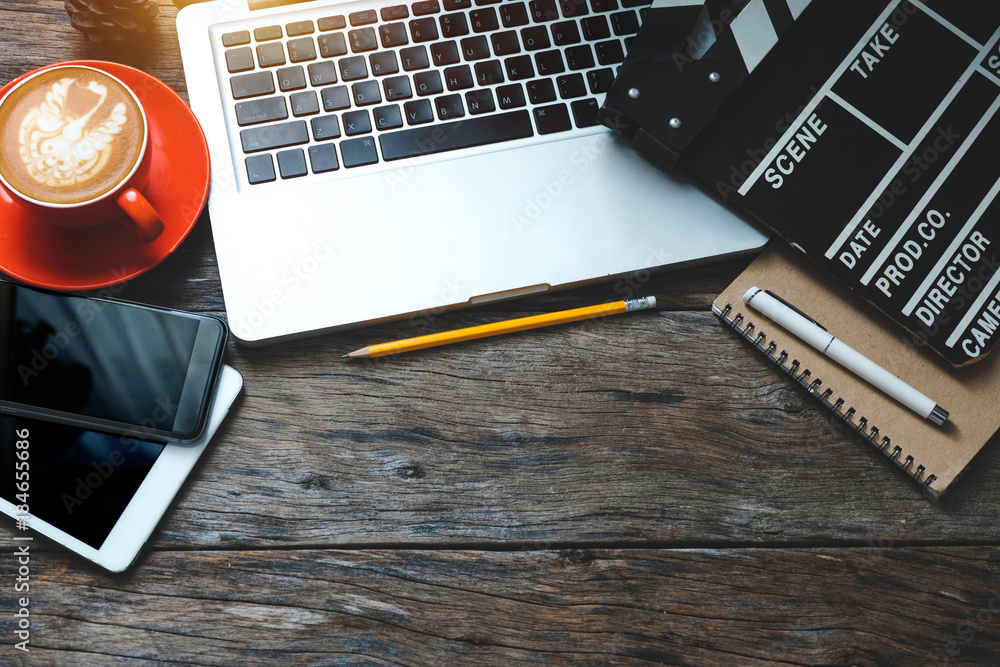 office stuff with Movie clapper laptop and coffee cup pen notepad on the wood table top view shot.
