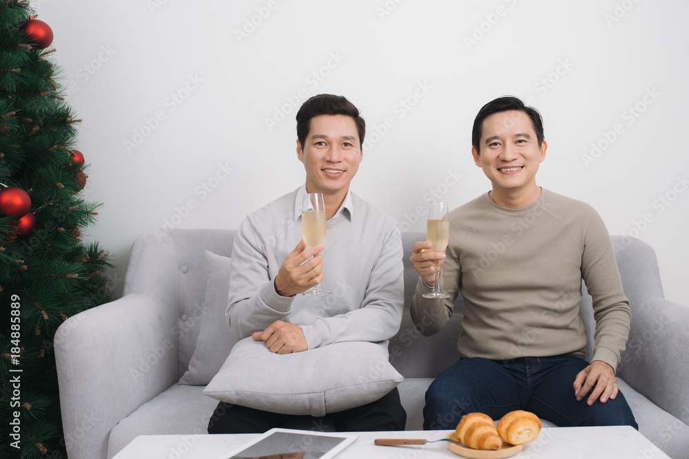 Two asian men wearing sweater holding champagne glass at home during christmas