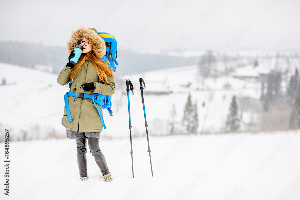 一个穿着冬装的女人在雪地里背着背包、跟踪棒和保温瓶徒步旅行的肖像