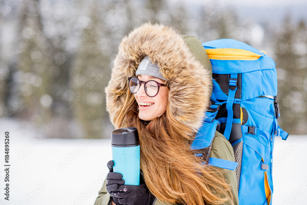 一个穿着冬装的女人在雪地里背着背包、跟踪棒和保温瓶徒步旅行的肖像