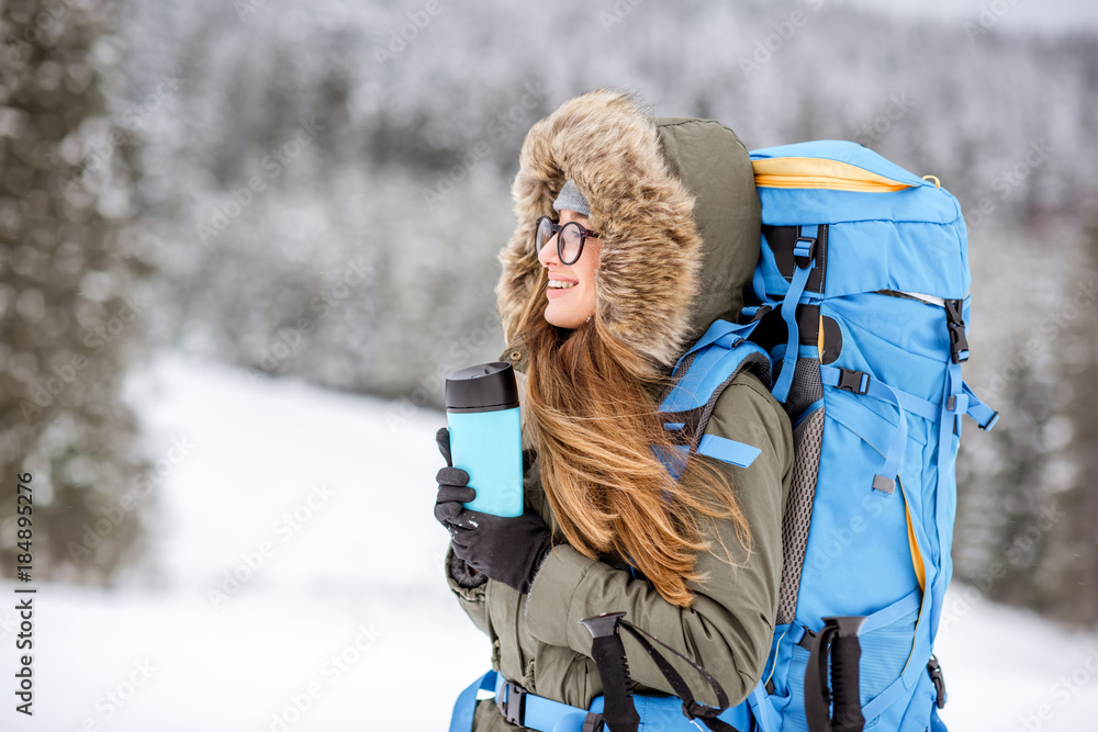 一个穿着冬装的女人背着背包、跟踪棒和保温瓶在雪地里徒步旅行的肖像