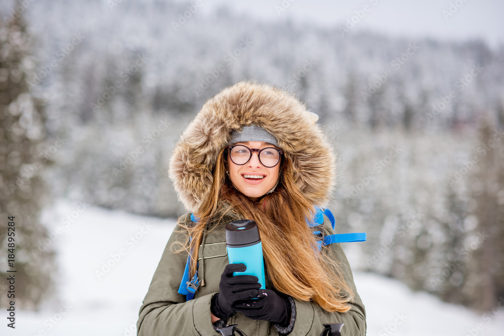 一个穿着冬装的女人背着背包、追踪棒和保温瓶在雪地里徒步旅行的肖像