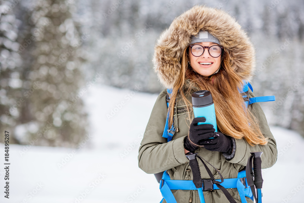 一个穿着冬装的女人在雪地里背着背包、跟踪棒和保温瓶徒步旅行的肖像