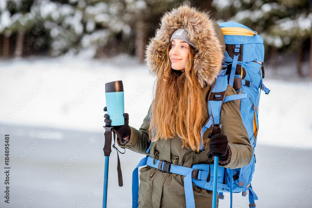 一位穿着冬装、背着背包、带着追踪棒和保温瓶在雪地里徒步旅行的女性的肖像