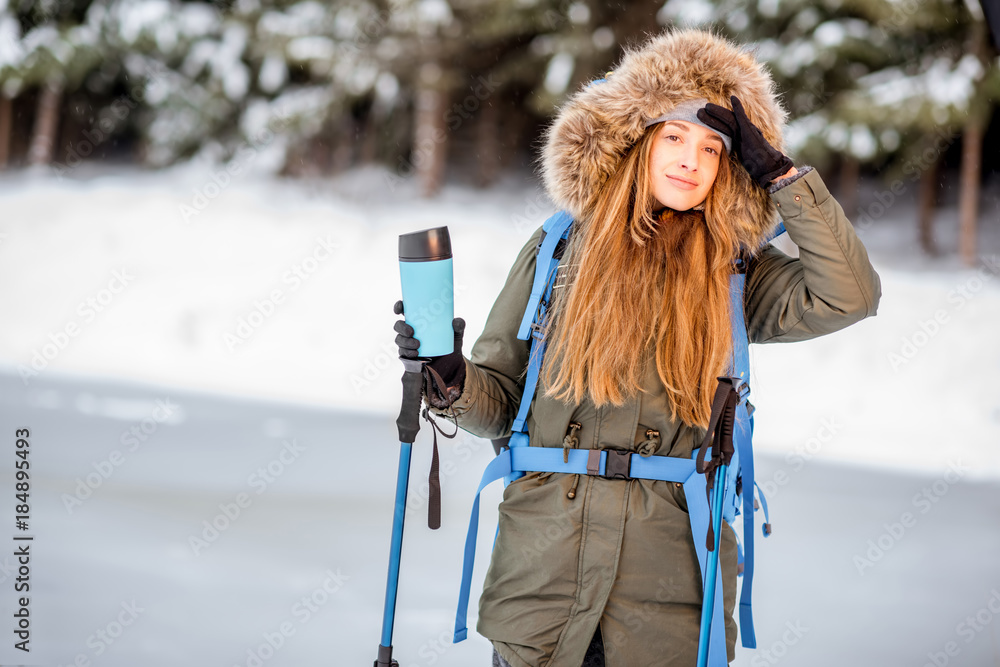 一个穿着冬装的女人背着背包、跟踪棒和保温瓶在雪地里徒步旅行的肖像