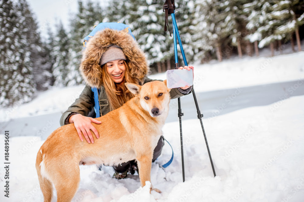 一名女子在冬季徒步旅行中休息，在附近的雪山与她的狗自拍