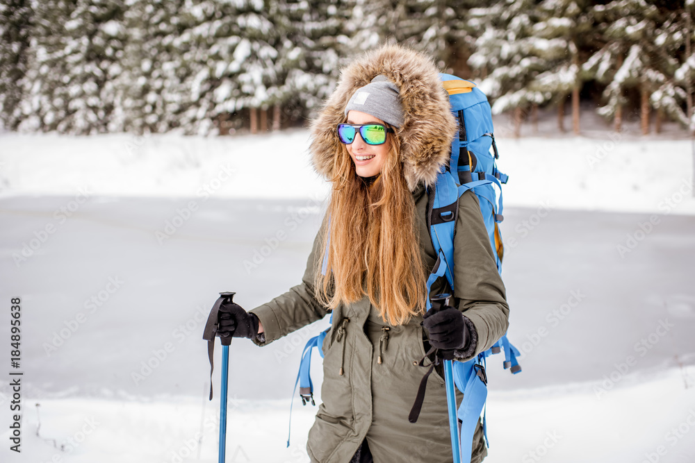 一位穿着冬装的妇女背着背包和追踪棒在雪地森林徒步旅行的肖像