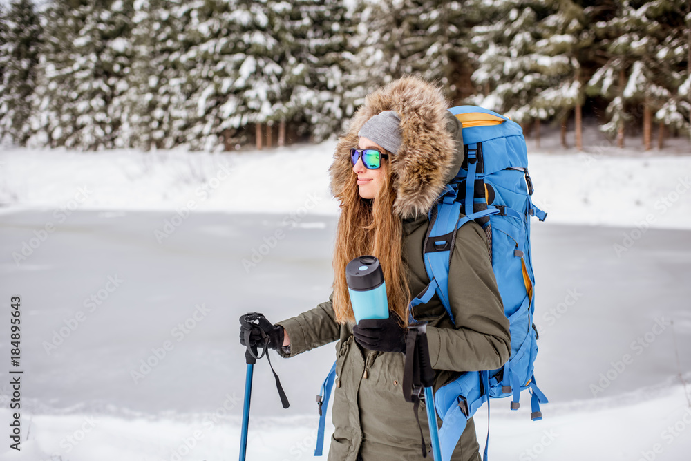 Portrait of a woman in winter clothes hiking with backpack, tracking sticks and thermos at the snowy