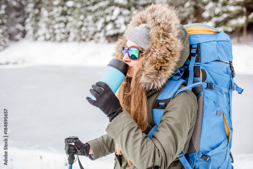 一个穿着冬装的女人背着背包、追踪棒和保温瓶在雪地里徒步旅行的肖像