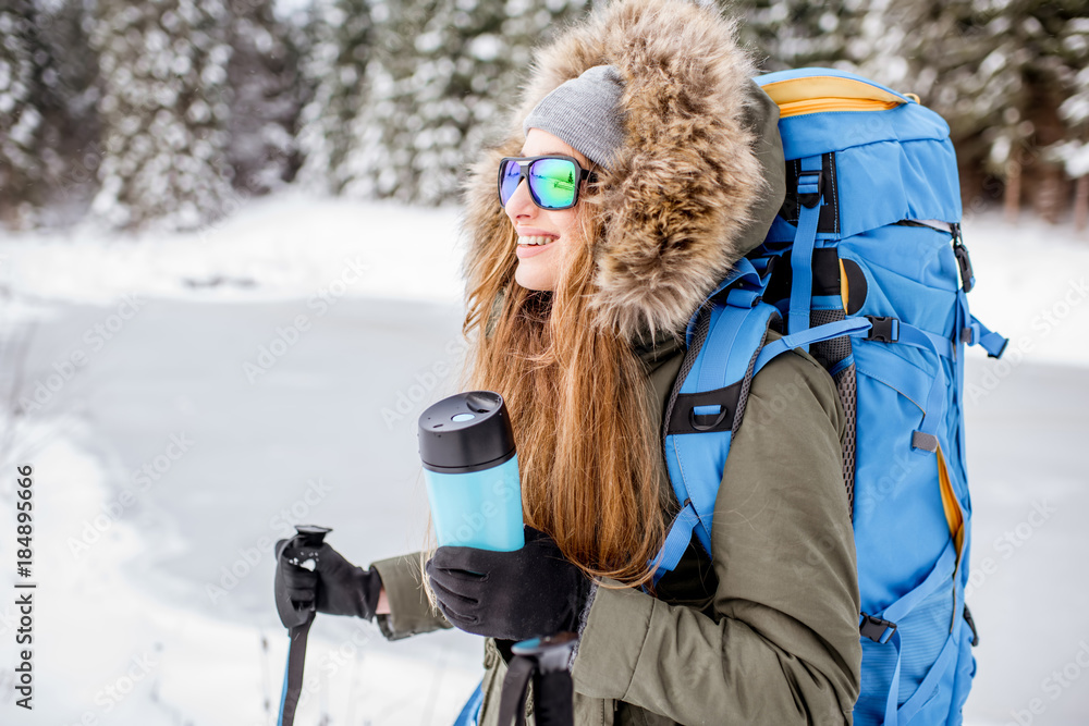 一个穿着冬装的女人在雪地里背着背包、跟踪棒和保温瓶徒步旅行的肖像