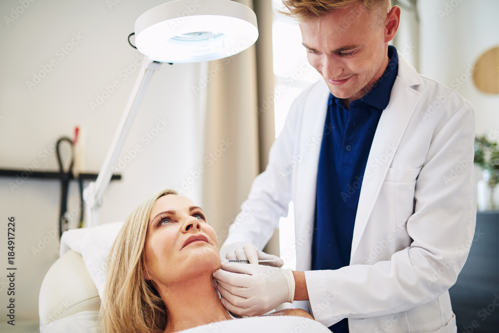 Smiling doctor performing injections on a mature clients face