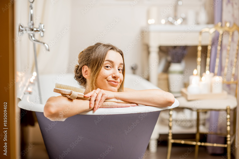 Portrait of a beautiful woman lying in the retro bath of the vintage bathroom decorated with candles