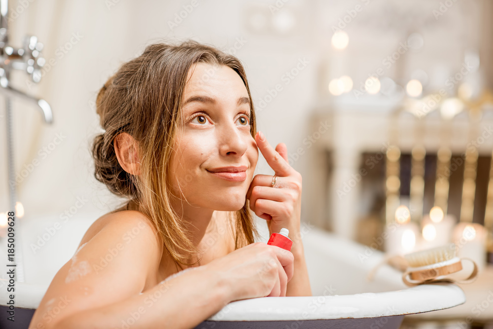 Young and pretty woman applying facial cream under the eyes in the bathroom