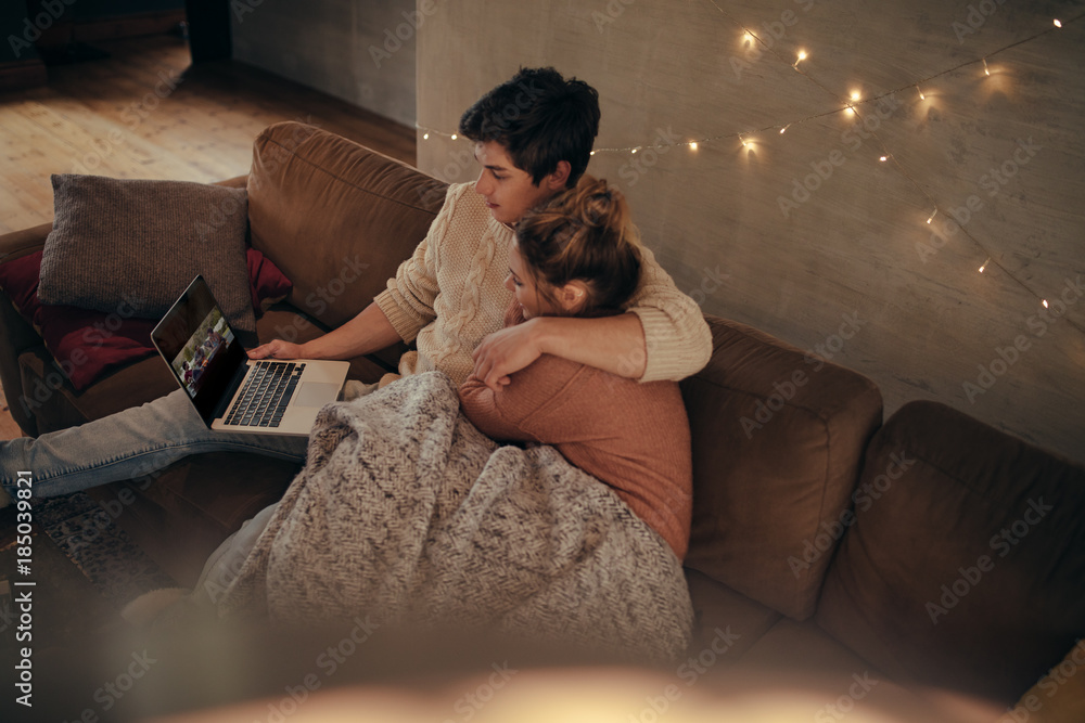 Cozy young couple sitting on sofa with laptop