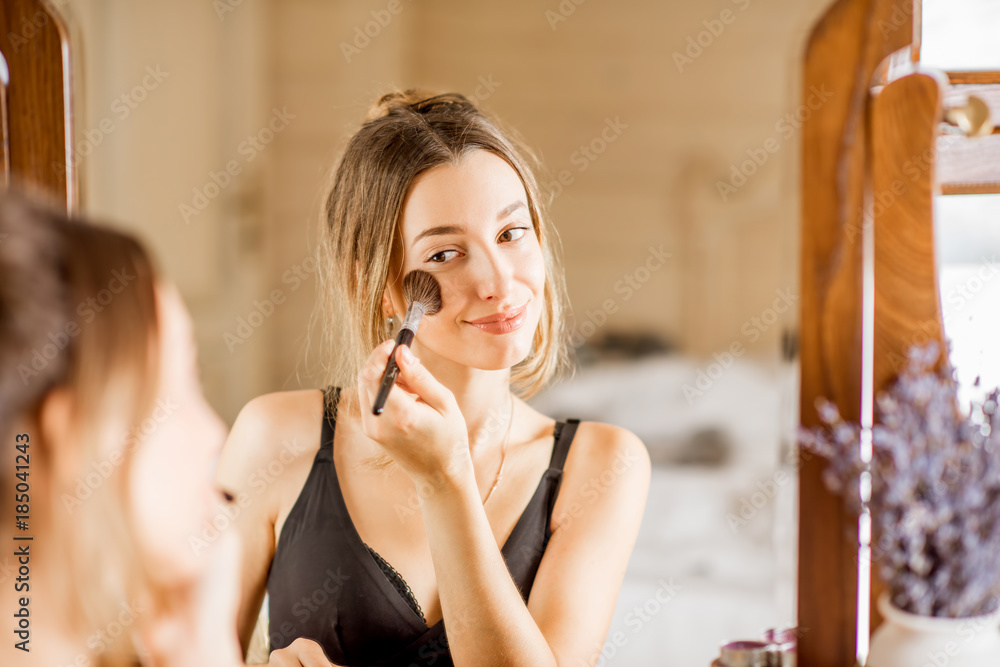 Young woman applying cosmetics with a brush sitting at the dressing table