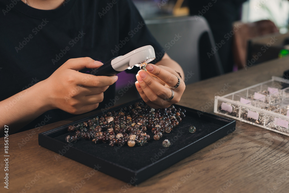 Hands of female jewelry designer looking at her work with magnifying glass