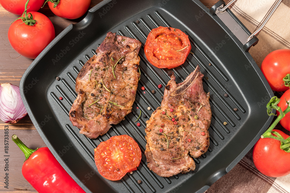 Grilled steak on grill pan with tomatoes on dark background