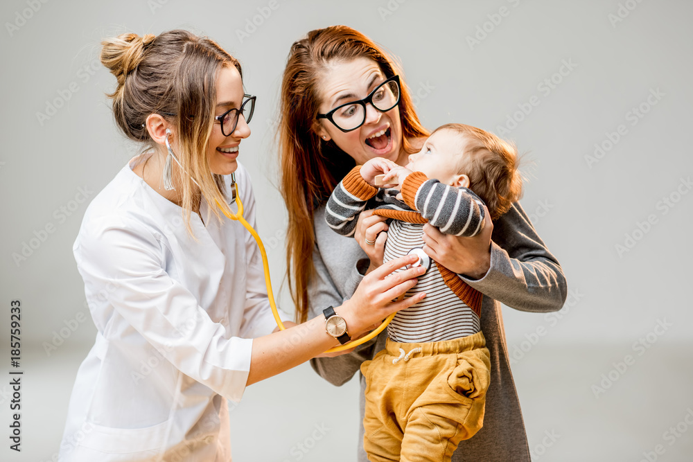 母亲带着她的男婴在年轻的女儿科医生面前，站在t处用听诊器听