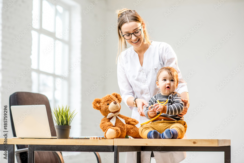 Young woman pediatrician taking care of a baby boy sitting on the table at the office