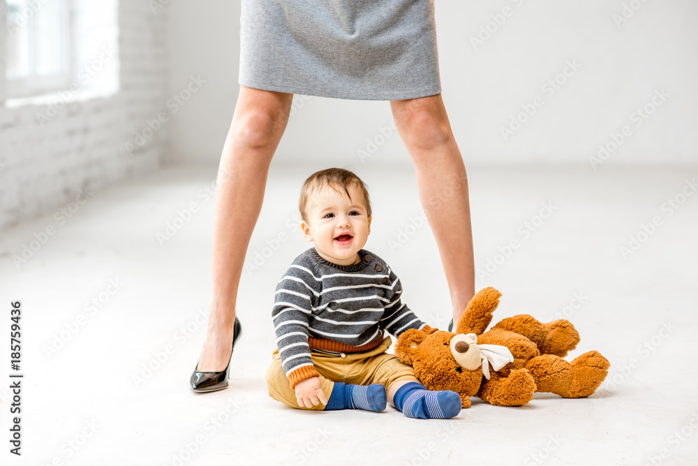 Baby boy playing near the womans beautiful legs sitting on the white floor