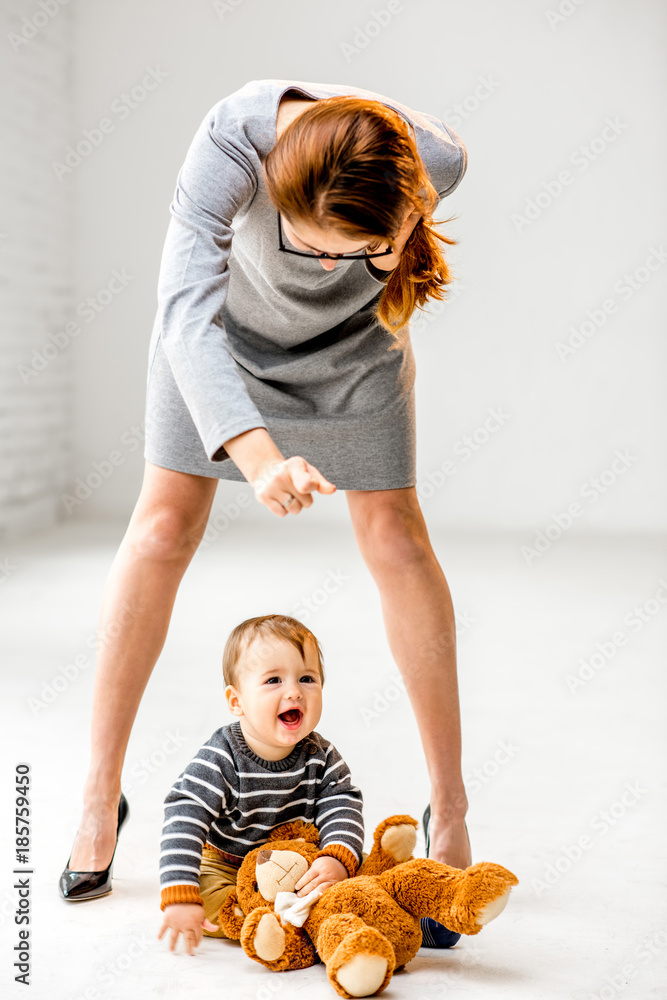 Baby boy playing near the womans beautiful legs on the white floor