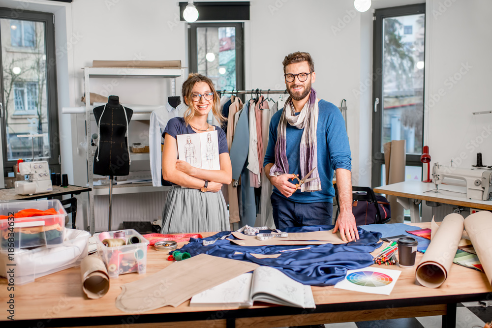 Portrait of a couple of fashion designers working with fabric and clothing sketches at the studio fu