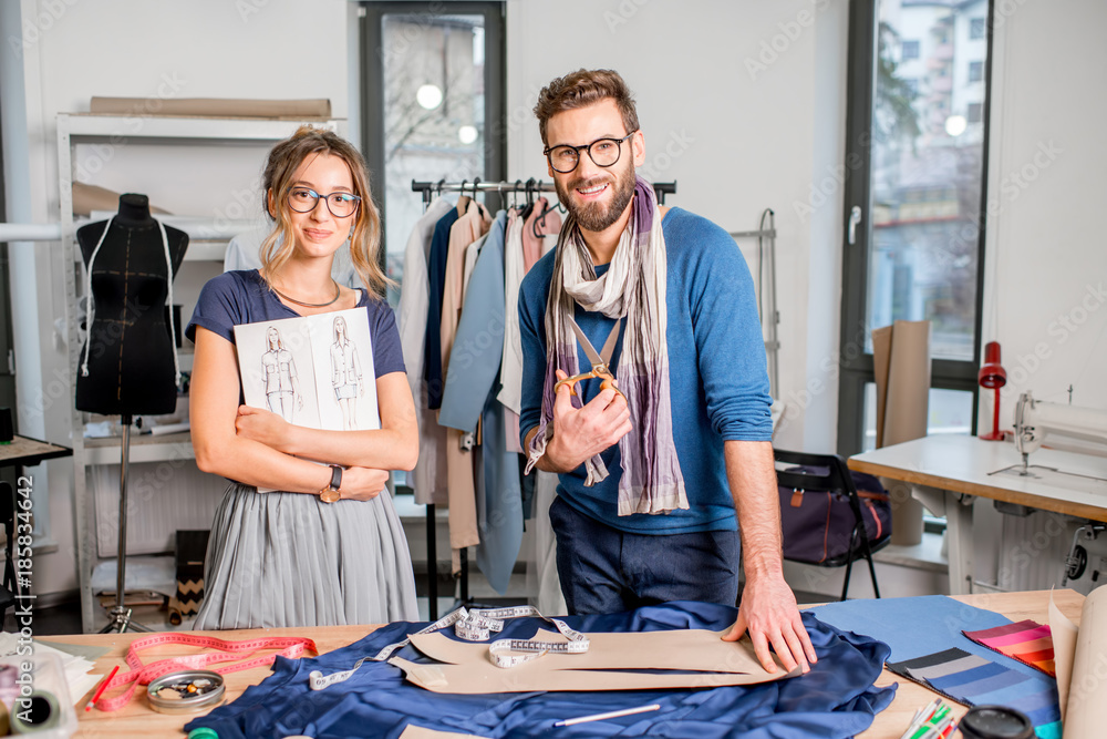 Portrait of a couple of fashion designers working with fabric and clothing sketches at the studio fu