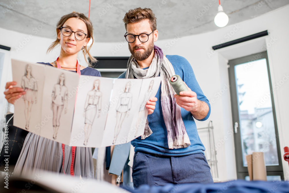 Couple of fashion designers working with clothing sketches at the studio