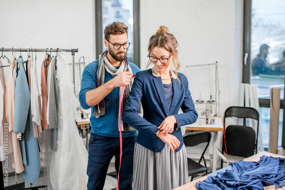 Handsome tailor measuring jacket on the woman client standing at the studio full of tailoring tools 