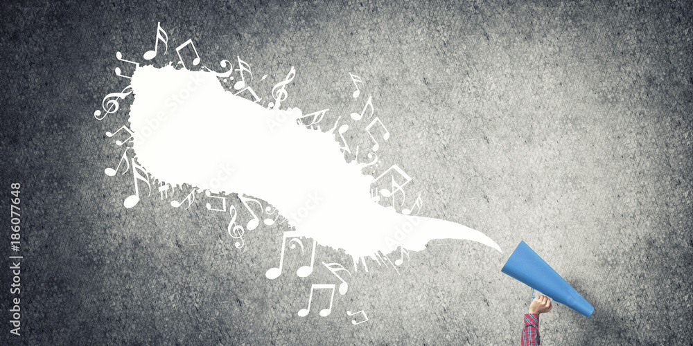 Hand of woman holding blue paper trumpet against concrete background