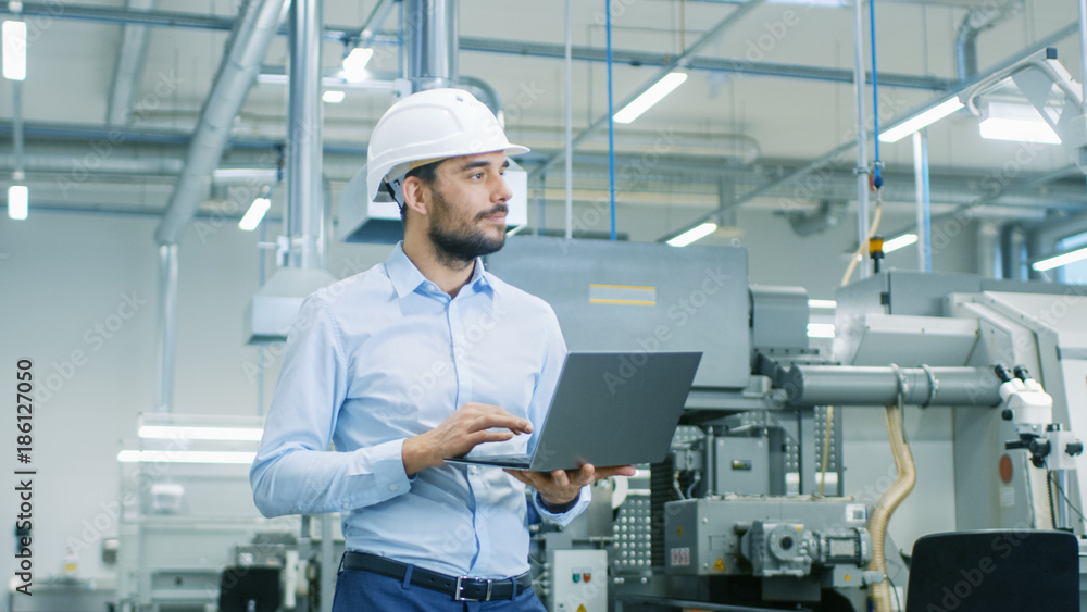 Chief Engineer in the Hard Hat Walks Through Light Modern Factory While Holding Laptop. Successful, 