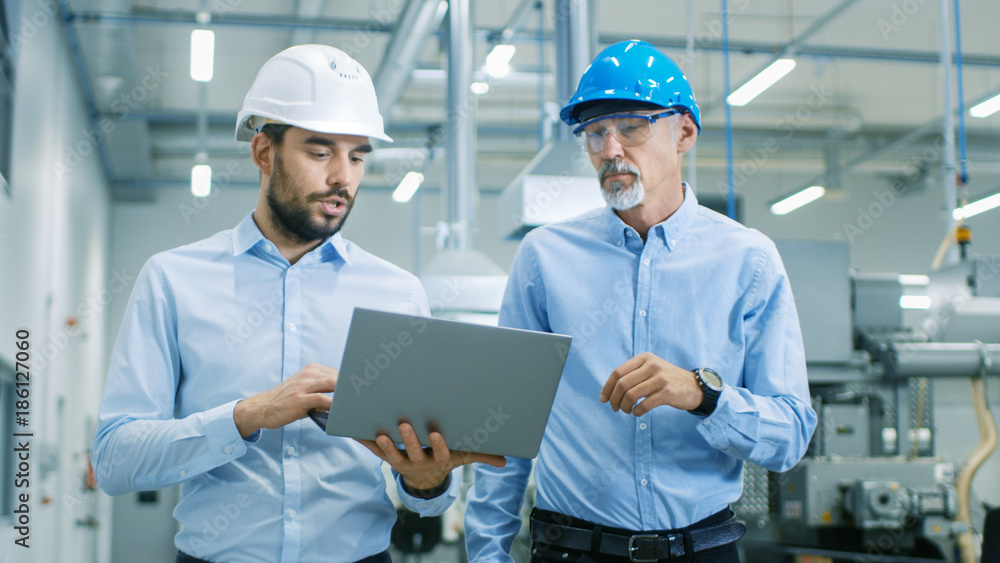 Head of the Project Holds Laptop and  Discusses Product Details with Chief Engineer while They Walk 