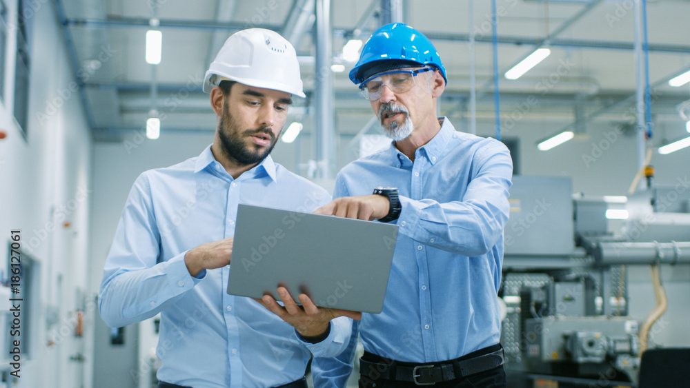 Head of the Project Holds Laptop and  Discusses Product Details with Chief Engineer while They Walk 