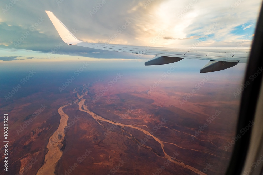 View from an aeroplane window over a red desert landscape with rivers. 