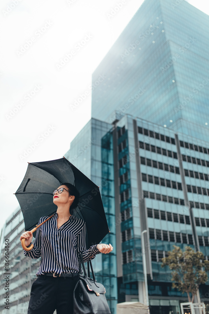 撑着伞走在城市街道上的年轻女商人