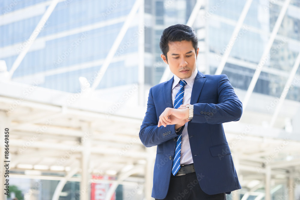 Confident businessman looking at his watch while standing outdoors with cityscape in the background