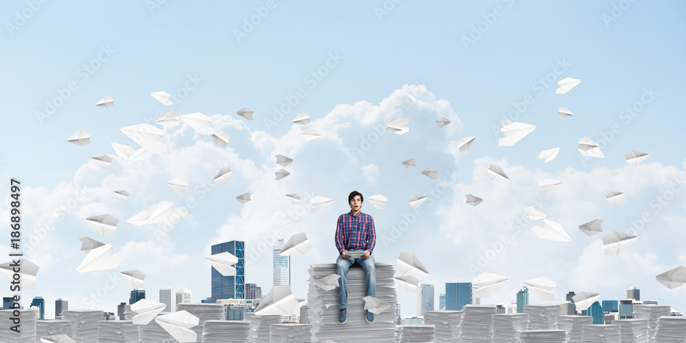 Attractive man sitting on pile of paper documents.